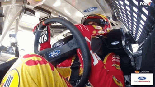 A Man In A Ford Racing Suit Is Sitting In The Driver 'S Seat Of A Race Car GIF