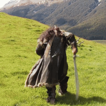 A Man In A Fur Coat Is Holding A Sword In A Field GIF