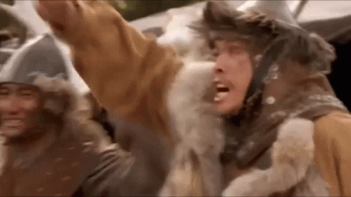 A Man In A Fur Coat Is Standing In Front Of A Crowd Of People With His Arms In The Air . GIF