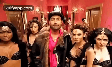 A Man In A Fur Coat Is Standing In Front Of A Group Of Women In Bras . GIF