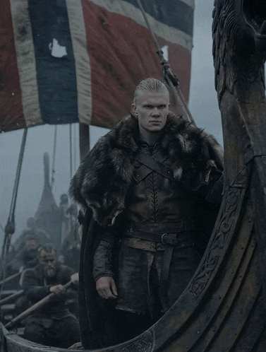 a man in a fur coat is standing on a viking ship