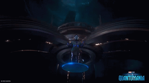 A Man In A Futuristic Suit Is Standing In A Dark Room With A Blue Circle Around Him . GIF