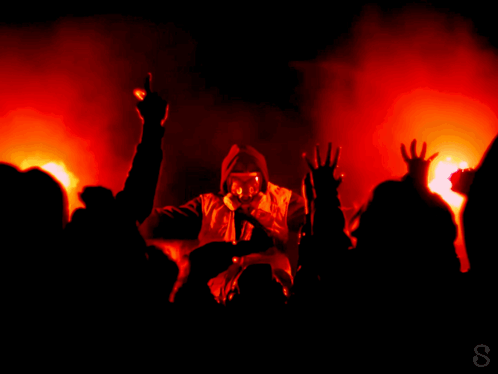 A Man In A Gas Mask Is Singing Into A Microphone In Front Of A Crowd Of People GIF
