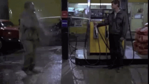 A Man In A Gas Mask Is Spraying Another Man With A Hose . GIF