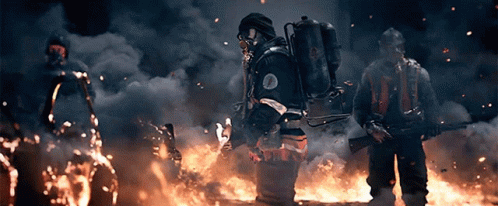 A Man In A Gas Mask Stands In Front Of A Large Fire GIF