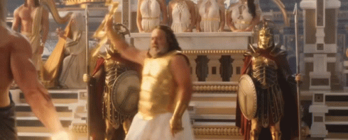 A Man In A Gold Armor Is Standing In Front Of A Statue Of A Greek God . GIF