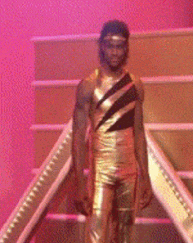 A Man In A Gold Leotard Is Standing On A Set Of Stairs GIF