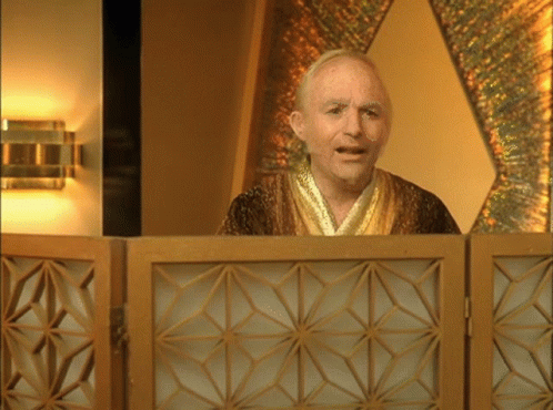 A Man In A Gold Robe Stands In Front Of A Wooden Screen GIF