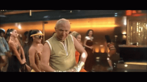 A Man In A Gold Tank Top Is Dancing In Front Of A Crowd Of Women GIF