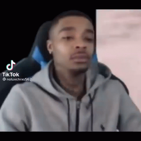 A Man In A Gray Hoodie Is Sitting In A Chair And Making A Funny Face . GIF