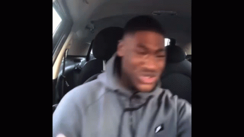 A Man In A Gray Hoodie Is Sitting In The Back Seat Of A Car . GIF