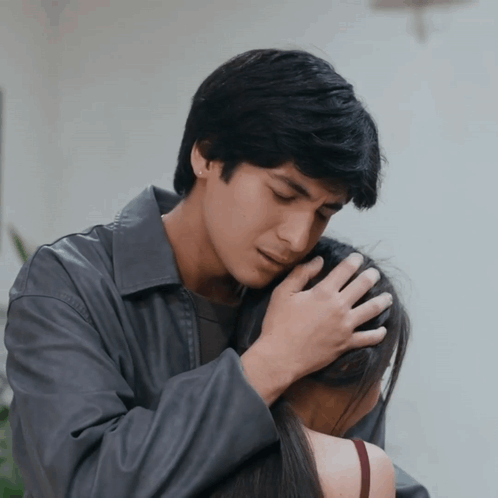 A Man In A Gray Jacket Holds A Woman In His Arms GIF