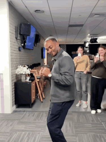 A Man In A Gray Jacket Is Dancing In A Hallway GIF