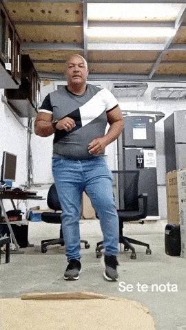 A Man In A Gray Shirt And Blue Jeans Is Dancing In A Room With The Words Se Te Nota Below Him GIF
