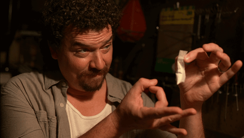 A Man In A Gray Shirt Is Holding A Piece Of Paper In His Hands GIF