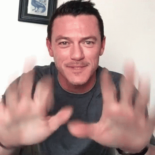 A Man In A Gray Shirt Is Holding His Hands Up In The Air . GIF