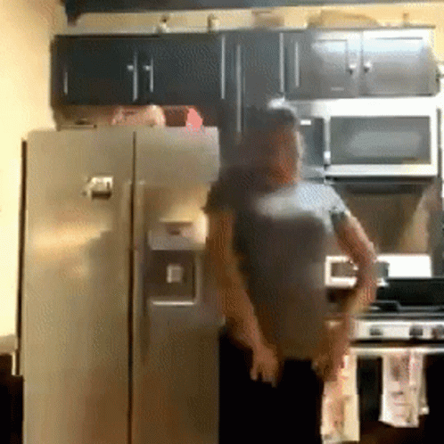 A Man In A Gray Shirt Is Standing In Front Of A Refrigerator In A Kitchen GIF