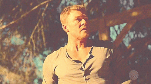 A Man In A Gray Shirt Is Standing In Front Of A Sign That Says Space GIF