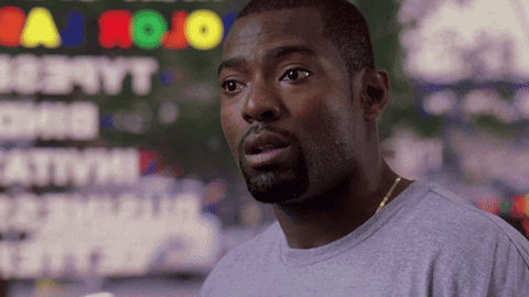 A Man In A Gray Shirt Stands In Front Of A Sign That Says Jojo GIF