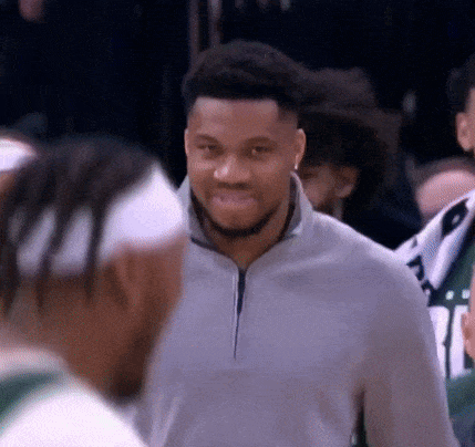 A Man In A Gray Sweater Is Smiling While Talking To Another Man . GIF