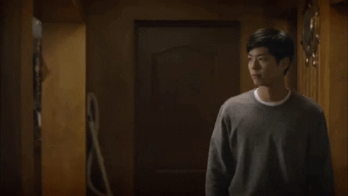 A Man In A Gray Sweater Is Standing In A Room And Talking To Someone . GIF