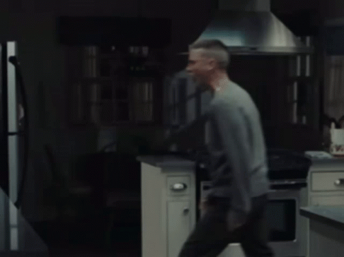 A Man In A Gray Sweater Is Standing In Front Of A Refrigerator GIF
