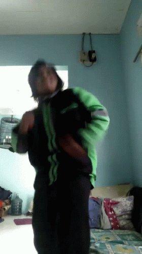 A Man In A Green And Black Jacket Is Dancing In A Living Room GIF