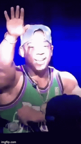A Man In A Green And Purple Jersey Is Waving At The Camera GIF
