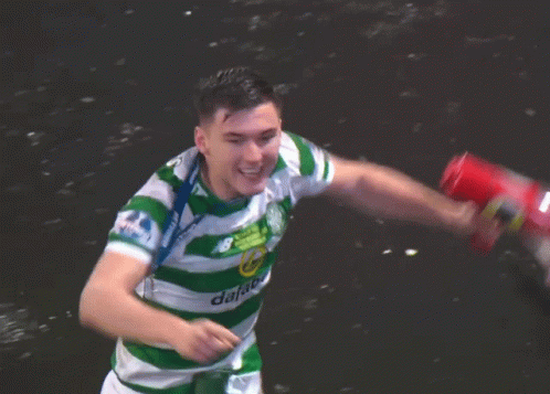 A Man In A Green And White Jersey With A Medal Around His Neck Holds A Red Can GIF