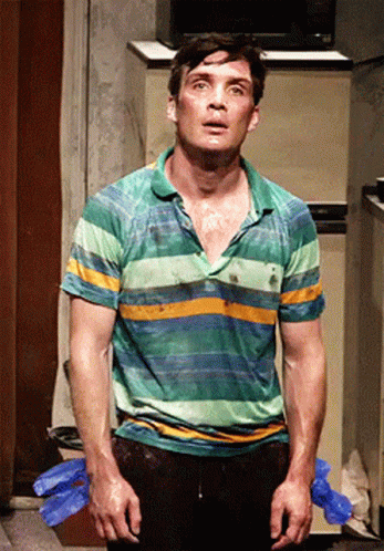 A Man In A Green And Yellow Striped Shirt Stands In Front Of A Refrigerator GIF