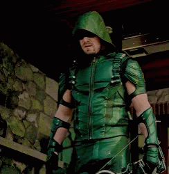 A Man In A Green Arrow Costume Is Holding A Bow And Arrows GIF
