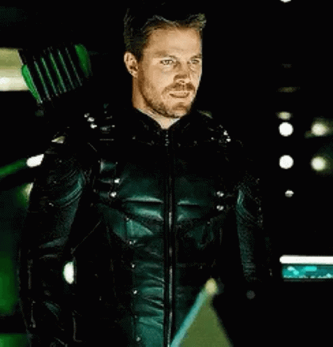 A Man In A Green Arrow Suit Is Holding A Green Arrow Behind His Back . GIF