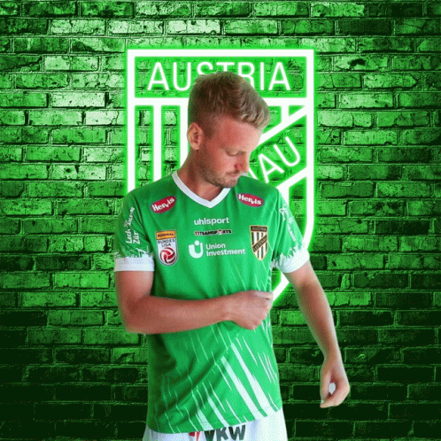 A Man In A Green Austria Jersey Stands In Front Of A Brick Wall GIF