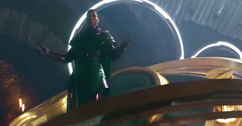 A Man In A Green Cape Is Standing In Front Of A Large Clock GIF