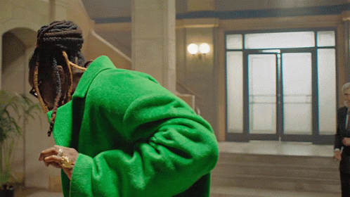 A Man In A Green Coat Stands In Front Of A Doorway GIF