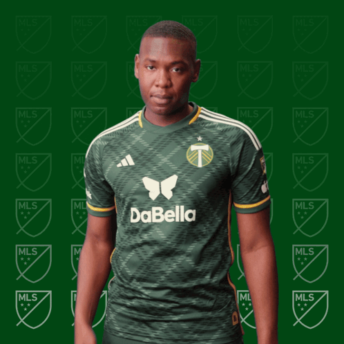 A Man In A Green Dabella Shirt Stands In Front Of A Green Background GIF