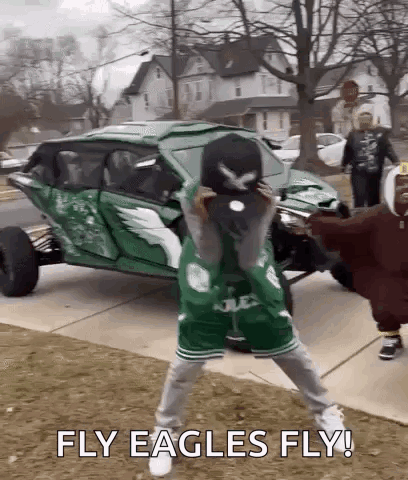 A Man In A Green Eagles Jersey Is Holding A Baseball Cap In Front Of A Green Vehicle . GIF