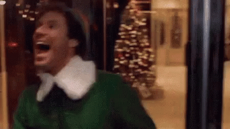 A Man In A Green Elf Costume Is Laughing In A Store Window . GIF
