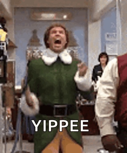 A Man In A Green Elf Costume Is Standing In A Room With His Mouth Open And Yipping . GIF