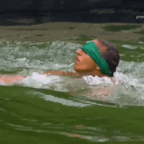 A Man In A Green Headband Is Swimming In A Body Of Water GIF