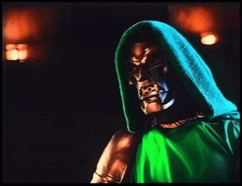A Man In A Green Hooded Cape Holds A Fist In The Air GIF