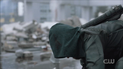 A Man In A Green Hooded Jacket Is Holding A Sword With The Letters Cw On The Bottom GIF
