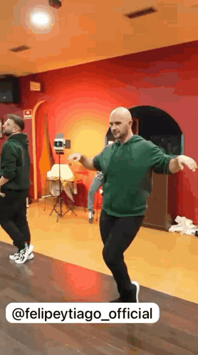 a man in a green hoodie is dancing in a room with a red wall behind him