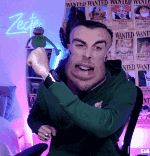 A Man In A Green Hoodie Is Sitting In Front Of Wanted Posters GIF