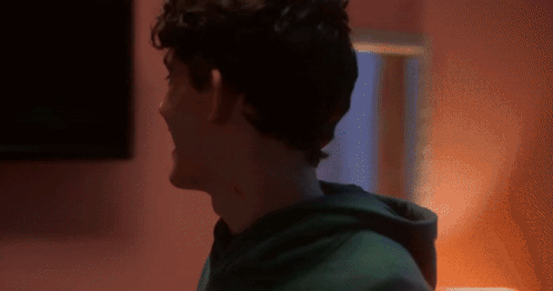 A Man In A Green Hoodie Is Standing In Front Of A Pink Wall GIF