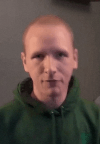 A Man In A Green Hoodie Looks At The Camera . GIF