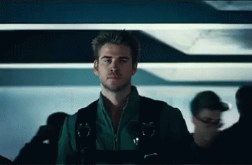 A Man In A Green Jacket And Black Vest Is Standing In A Crowded Room . GIF