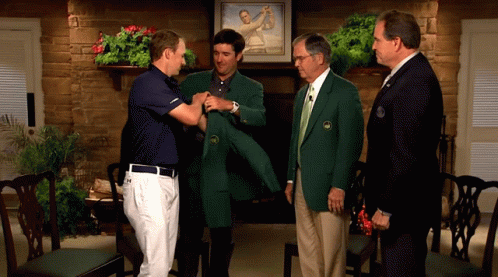 A Man In A Green Jacket Is Being Helped By Another Man In A Blue Shirt GIF