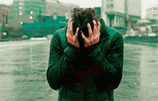 A Man In A Green Jacket Is Covering His Face With His Hands . GIF