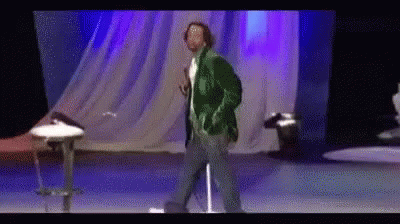 A Man In A Green Jacket Is Dancing On A Stage . GIF